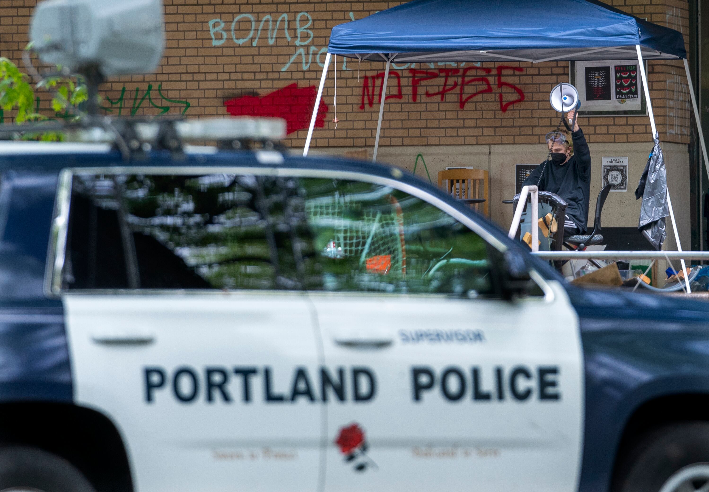 A protester sits in front of Portland State University’s Branford Price Millar Library, May 2, 2024, and plays a N.W.A. song titled “F**k tha Police,” as law enforcement announces they will be taking action. People protesting Israel's role in the war in Gaza had occupied the library since Monday evening.