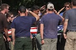 Several people salute the body of a firefighter who was killed while others carry the body on a stretcher. An American flag is draped over the body.