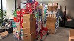 Pictured is the corner of an office, filled with boxes of diapers, toilet paper and other hygienic goods. Brands that can be see are Huggies in it's red box, Pampers in it's aqua blue and several unlabeled brown boxes. The piles of the boxes reach the ceiling and take up a good portion of the room.