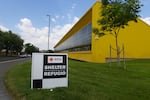 A sign reading "shelter" in both English and Spanish is posted in front of a bright yellow school building.