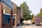 Workers watch as equipment is unloaded to prepare to demolish the Bend Senior High School auditorium, pictured left in Bend, Ore., on July 22, 2024.