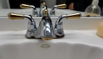 A silver and gold faucet above a sink shows signs of corrosion near its base.