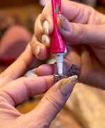 A close up of a hand with golden-painted fingernails, applying glue to a false eyelash.