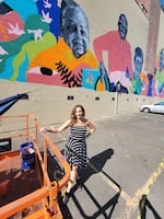 Executive Producer, Zoe Piliafas, stands in front of a colorful mural.