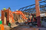 Two people stand on top of a partially disassembled wall while a large construction crane is parked inside the frame of a gutted brick building.