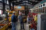 Frank Kemp, maintenance coordinator for the Astoria Riverfront Trolley at center, and Mark Stover, trolley Operations and Safety Committee chair, discuss repairs as the trolleys sit parked in the maintenance and storage garage in Astoria, Ore., on Feb. 12, 2026.