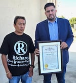 Carlitos Ricardo Parias (left) receives a certificate of recognition from Jose Ugarte, chief of staff for Los Angeles City Council member Curren Price, in Los Angeles in August 2025.
