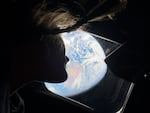 Astronaut and Artemis II mission specialist Christina Koch peers out of one of the Orion spacecraft's main cabin windows, looking back at Earth, as the crew travels towards the Moon.