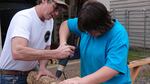 Shop teacher Chris Mathas helps Kaden Delatorre drill holes in an oak log.