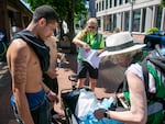 Javonte J. (last name withheld for privacy), left, receives water from Transition Projects team member Bess Turner, right, while outreach supervisor Tara Slak, middle, passes out informational flyers near Union Station, Portland, Ore., July 5, 2024. Transition Projects serves people experiencing homelessness — who are some of the most vulnerable to extreme weather — year-round. 