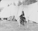 "Small Hawk in Native Dress with Ornaments and Bag, On Horseback; Tipi Nearby 1900"