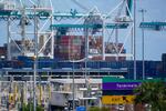 Very large industrial cranes loom over stacked containers with an enormous ship   filled with containers visible in the background.