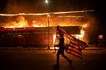 A person carrying an upside-down U-S flag runs at night, with a burning building in flames behind them.