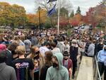 A crowd of students wearing face masks gathers around a flag pole outside.