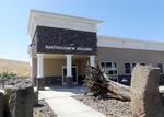 A small, modern-looking office building is foregrounded by a large piece of decorative wood and several stones.