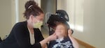 A mom with mask is touching the face of a child who is sitting on a stroller.