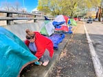 FILE - A young woman secures a tarp on her tent along SW 13th Avenue in Portland, April 4, 2022.