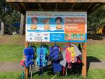 A wooden structure in a park that reads "Life Jacket Loaner Station," with several life jackets hanging on it