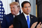 President Donald Trump walks past Secretary of State Marco Rubio. There's a U.S. flag behind them.