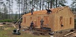 A construction crew builds a frame of a new house in a forested area.
