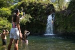 Tourists jump into a pool of water next to a waterfall at Pua'a Ka'a State Wayside Park.