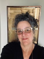 A woman with gray hair, glasses and a black shirt smiles for a selfie.