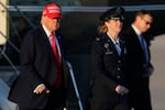 President Donald Trump, left, gestures as is escorted by Air Force Col. Angela Ochoa, commander of the 89th Airlift Wing, center, as he walks from Marine One before boarding Air Force One, Friday, Feb. 28, 2025, at Joint Base Andrews, Md.