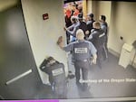 A screen capture from a video shows people in law-enforcement uniforms attempting to guard a door as a crowd surges against them and tries to gain entry