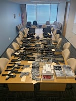 A table in a conference room is covered with guns and gun parts seized by law enforcement.
