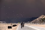 Bike riders make their way along the coast as large dark plume of smoke passes over the beach from a wildfire.