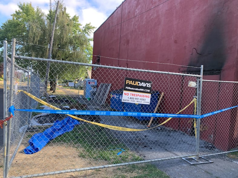 Chain-link fencing can be seen on the side of the Roseway Theater in Northeast Portland. A portion of the building is charred from a recent fire.