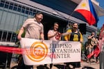 Celebrants cut a red ribbon at the grand opening of Portland's Filipino Bayanihan Center in June 2021. Three people are pictured in front of a small building holding a banner that reads "FILIPINO BAYANIHAN CENTER." Behind them hangs a Filipino flag. One woman holds large scissors which she's just used to cut a red ribbon across the front of the building's entrance.