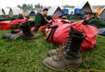 In this Aug. 25, 2015, file photo, Mac Mega, center, rests with fellow firefighters from Oregon-based Grayback Forestery, at a camp for firefighters battling the Okanogan Complex Fire in Okanogan, Wash. Empty cow pastures on one day can be bustling with hundreds of firefighters the next as fire camps with colorful tent cities spring up.  Truckloads of supplies and equipment are needed to keep wildland firefighters effective at fighting flames for weeks on end. The size of each camp is determined by the size and complexity of the wildfire.