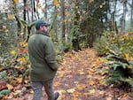 A man in a green jacket and green hat walks through the forest.