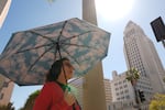 A pedestrian holds a cloud themed umbrella under a sunny day next to Los Angeles City Hall in Los Angeles Thursday, March. 12, 2026.