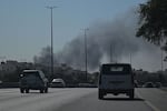 Motorists drive along a street as smoke rises from a reported Iranian strike in the area where the U.S. Embassy is located in Kuwait City on March 2, 2026.