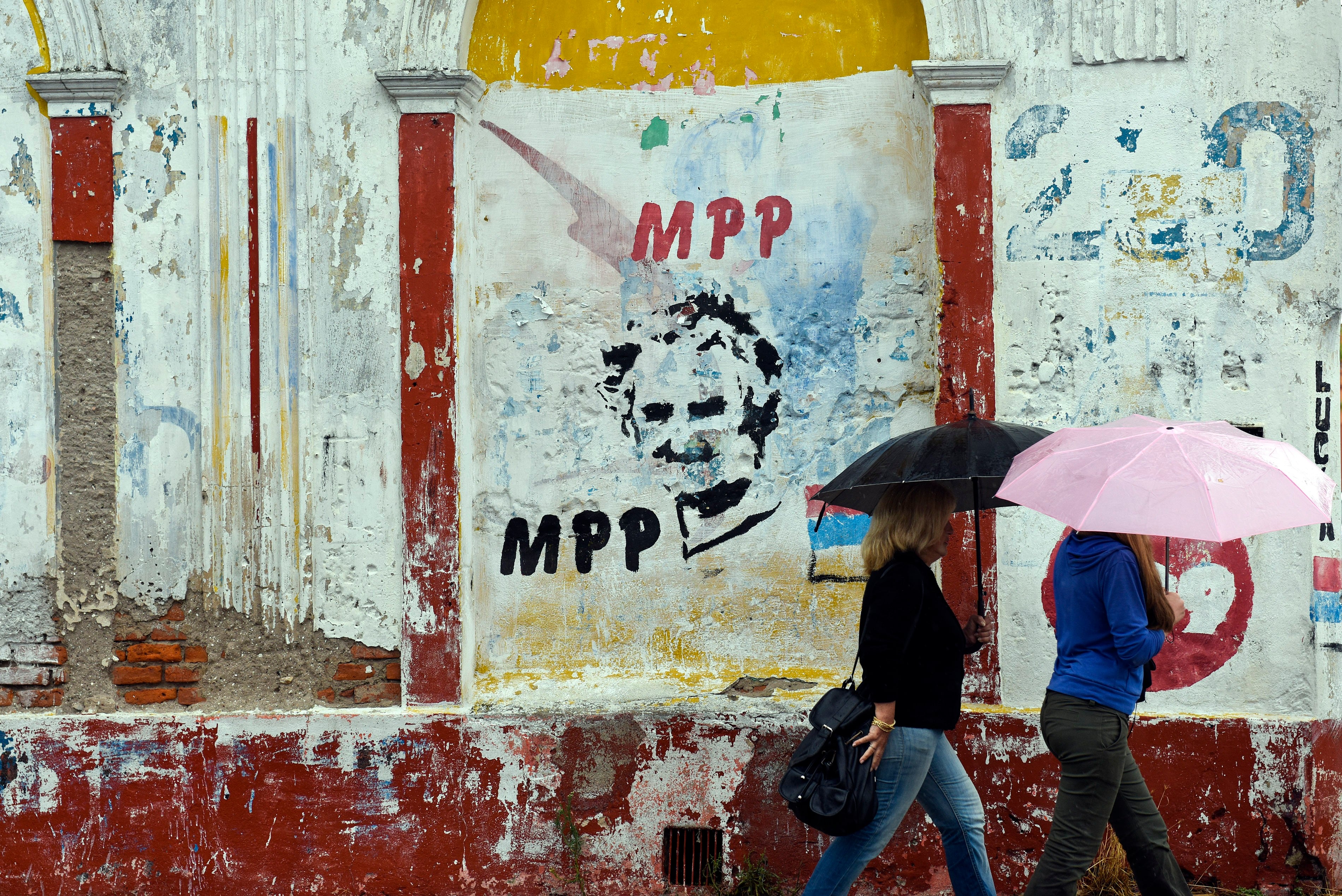 People walking in the rain pass by an image of Uruguay's then-president, José Mujica, during the presidential runoff election in Canelones, Uruguay, on Nov. 30, 2014.