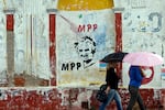 In this 2014 photo, two women holding umbrellas walk by an image of Uruguay's then-president, José Mujica, that's painted on a wall outdoors.