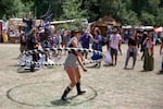 A woman attracts a small crowd while performing a demonstration with an oversized hula hoop.