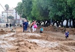 TOPSHOT - Family members walk on a mud-covered road in a flooded area in Picanya, near Valencia, eastern Spain, on October 30, 2024. Floods triggered by torrential rain in Spain's eastern Valencia region have left 51 people dead, according to emergency services on October 30. (Photo by Jose Jordan / AFP) (Photo by JOSE JORDAN/AFP via Getty Images)