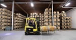 A forklift carries barrels of win around a warehouse with stacks of barrels of wine in the background.