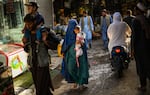 In this picture taken on July 20, 2022, a woman wearing a traditional burqa and carrying a child walks through a market in Kabul. The country still heavily relies on aid.