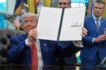 In this photo, President Trump holds up an executive order he signed. He's seated at a desk in the Oval Office of the White House on May 23, 2025.