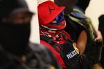 Federal agents wearing masks patrol the halls of the immigration court at the Ted Weiss Federal Building in New York City on July 9. The agent in the center of the photo is wearing a red baseball cap with the Air Jordan logo on it, sunglasses with blue lenses, a red and blue bandana that covers the face, a red shirt and a black vest that says "POLICE" on the front.
