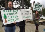 Opponents of a plan to sell the Elliott State Forest hold signs outside an Oregon State Land Board meeting.