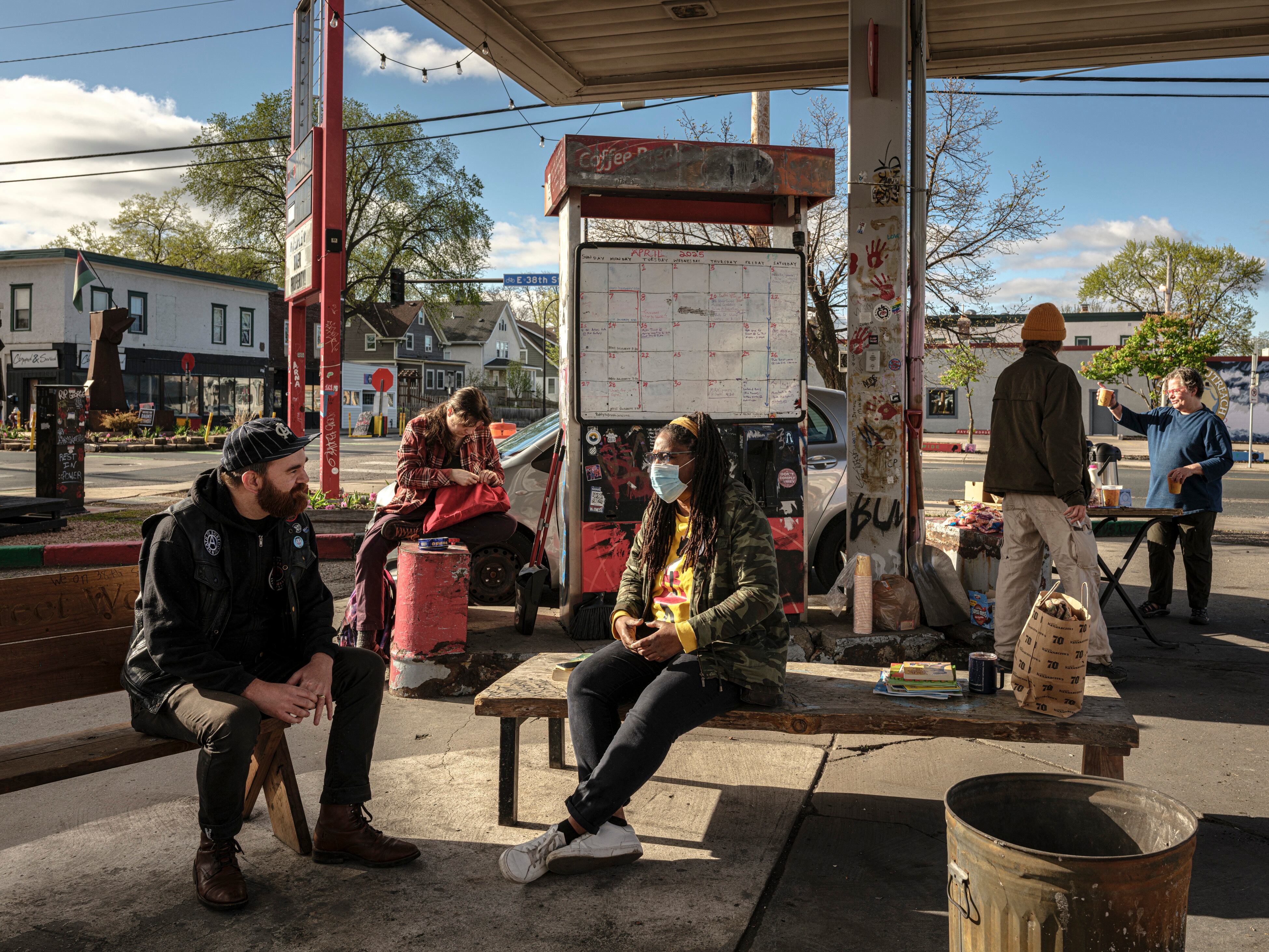 Marcia Howard, seated at center, speaks with another community member at George Floyd Square. Activists say they have gathered here every morning for the last five years.