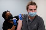 A person in protective medical clothing administers a vaccine to a person wearing a mask.