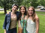 Three eighth grade students embrace and smile at the camera while posing for a photo outside.