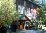 An old wooden hotel is bathed in sunlight on a bright morning. A sign celebrating the 100th anniversary of the Wallowa Lake Lodge hangs above the entrance.