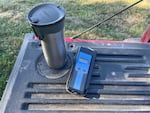 An insulated beverage container and digital thermometer sit on the tailgate of a pickup truck.